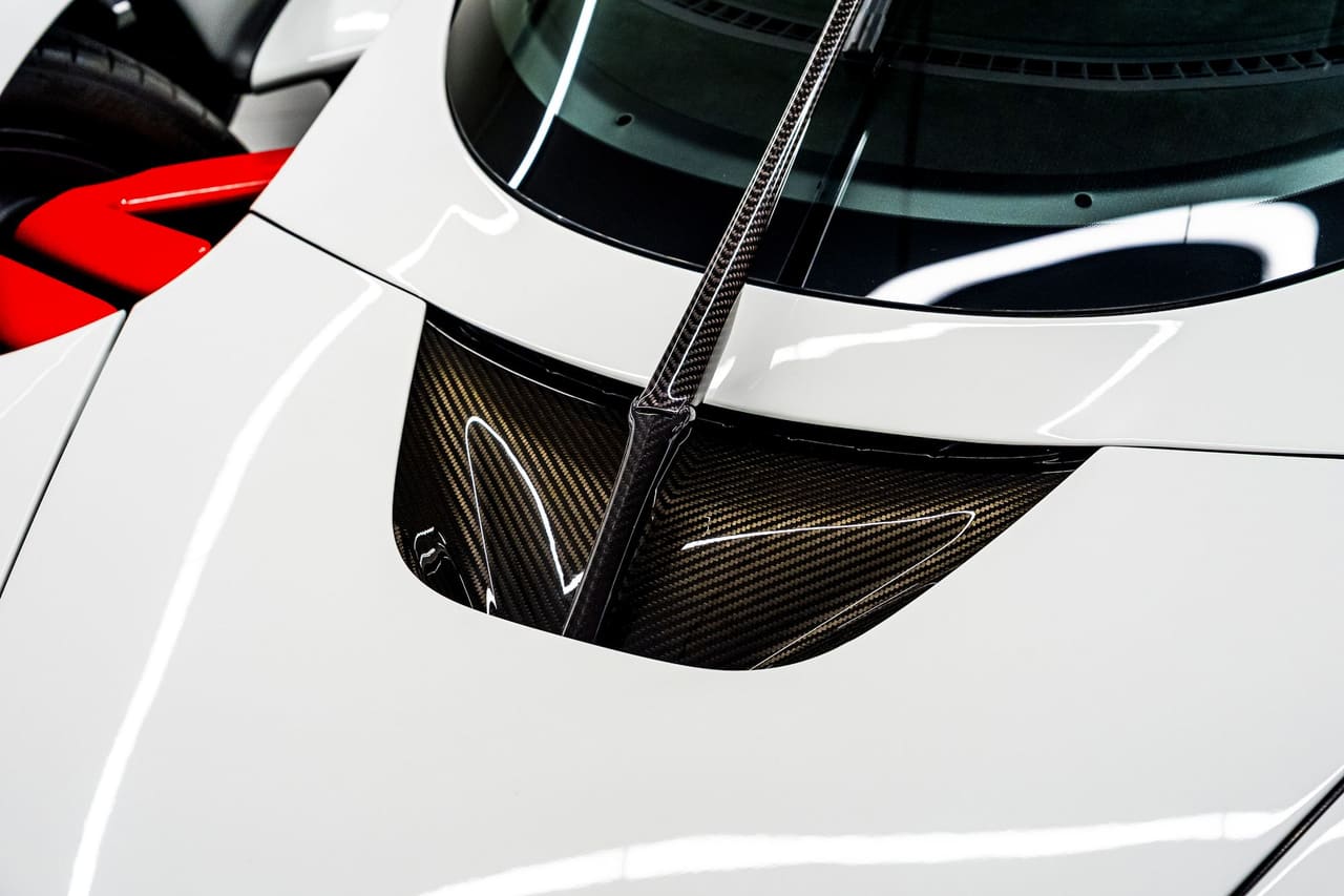 Close-up of the white bodywork of an Aston Martin Valkyrie beside the cockpit, where an opening lined in exposed carbon fibre lets air pass through the body