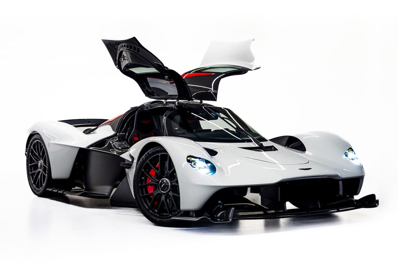 A white Aston Martin Valkyrie from the front three-quarter with both doors raised, showing how each door lifts away with part of the roof