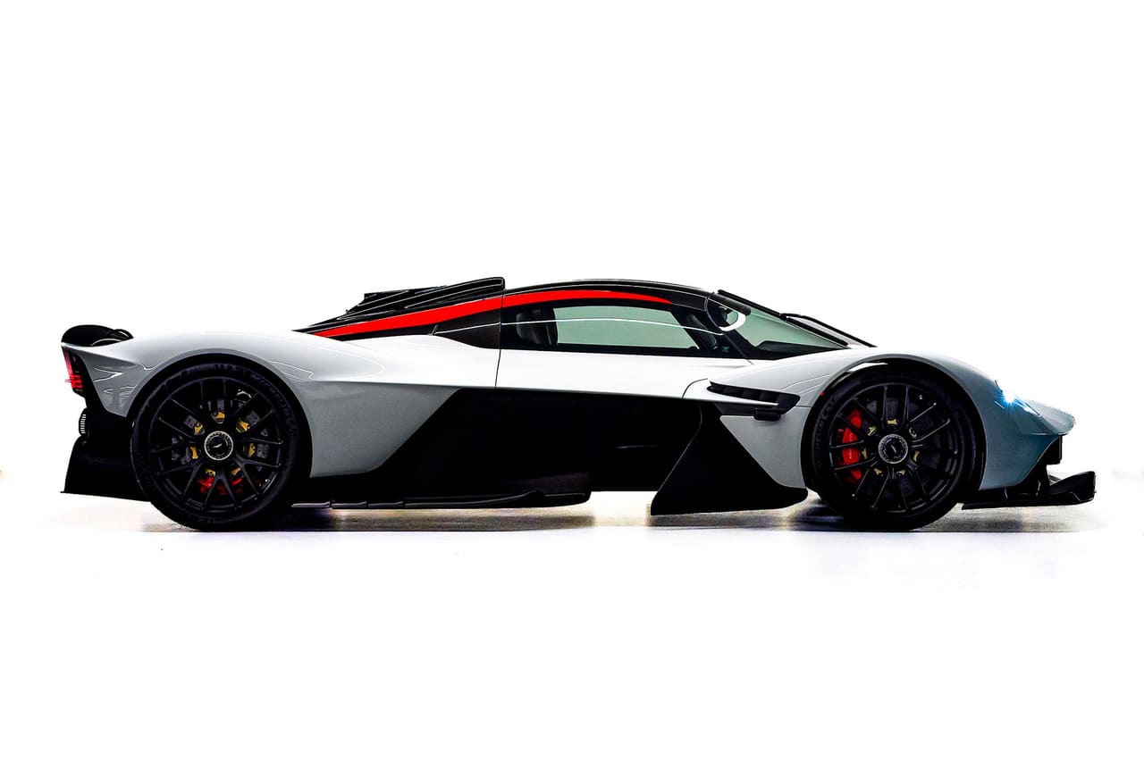 A white Aston Martin Valkyrie in profile on a white studio floor, its teardrop cockpit marked with a red stripe and the bodywork cut away behind the front wheels