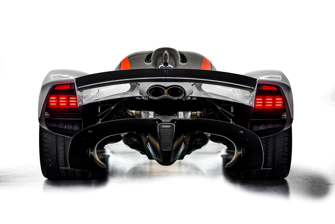 The rear of a white Aston Martin Valkyrie, straight on: red light blades either side, the wing across the top, twin exhausts high in the centre and the diffuser sweeping up beneath, with red stripes over the engine cover