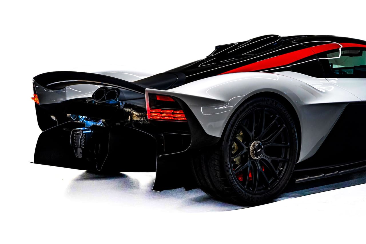 A white Aston Martin Valkyrie from the rear three-quarter, with the red stripe running back over the roof to the engine cover and the open bodywork around the rear wheel