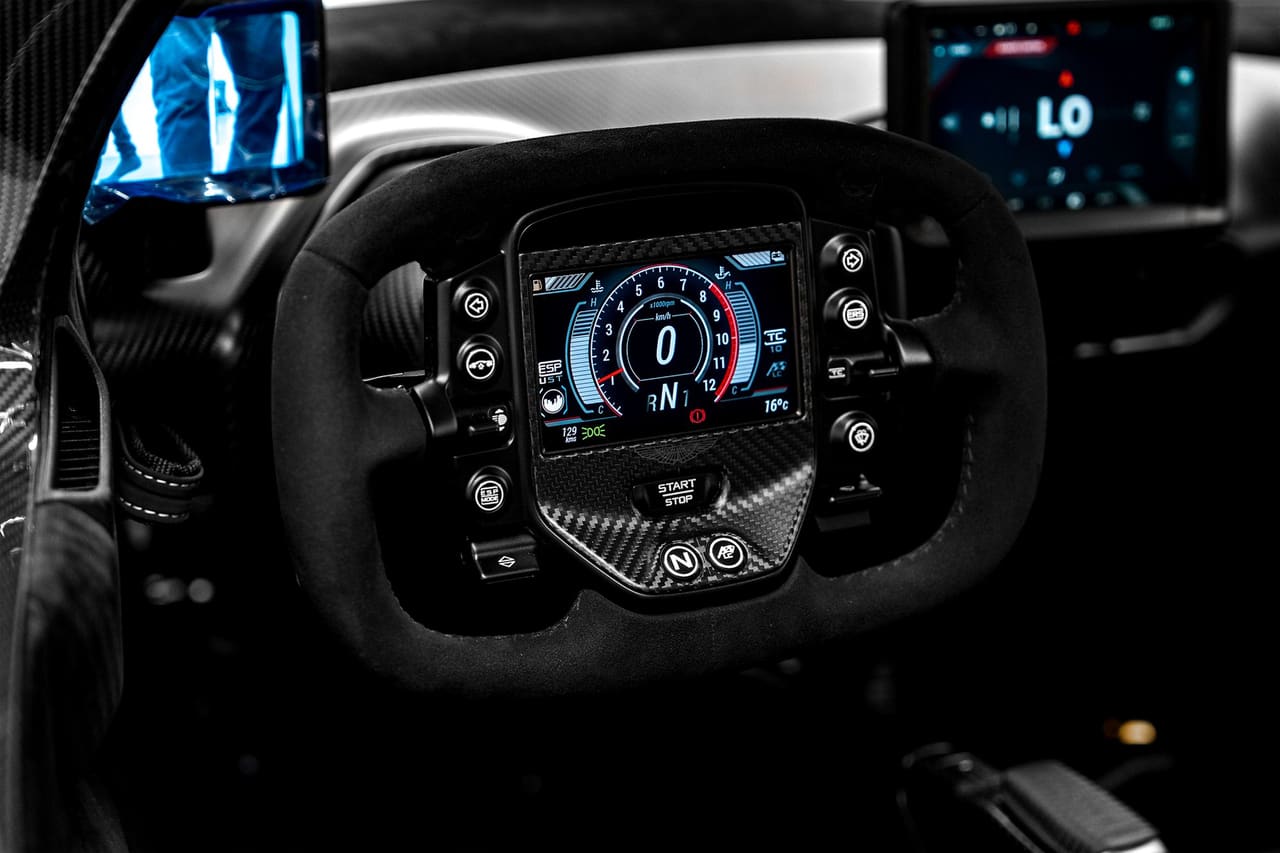 The Aston Martin Valkyrie steering wheel, flat-topped and trimmed in black, with a digital display at its centre surrounded by buttons and rotary controls