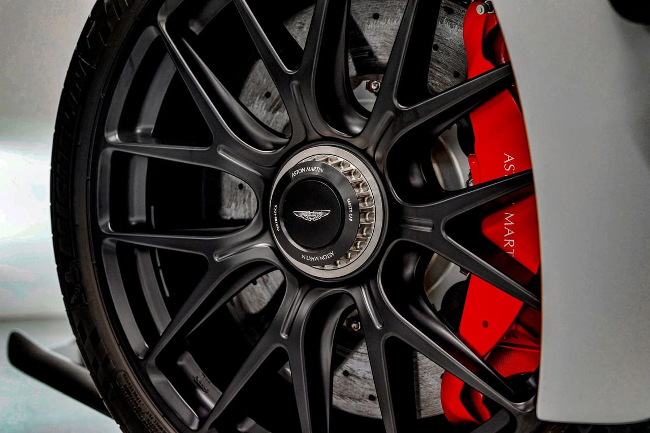Close-up of an Aston Martin Valkyrie wheel in satin black with a single central locking nut, in front of a red brake caliper and a ventilated carbon-ceramic disc